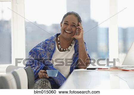 Stock Image - Indian businesswoman drinking coffee at desk. Fotosearch