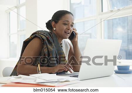 Indian businesswoman using cell phone at desk View Large Photo Image Picture - Indian businesswoman using cell phone at desk. Fotosearch