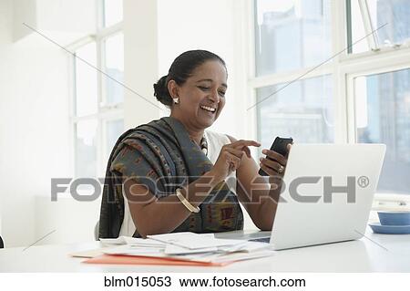 Stock Image - Indian businesswoman using cell phone at desk. Fotosearch