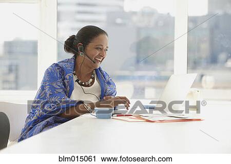 Stock Image - Indian businesswoman using headset at desk. Fotosearch