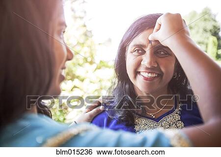 Stock Photograph - Indian woman putting jewel on mother's forehead. Fotosearch