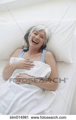 Stock Image - Laughing Caucasian woman laying in bed. Fotosearch