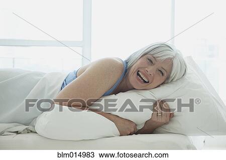 Stock Image - Laughing Caucasian woman laying in bed. Fotosearch