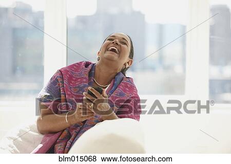 Stock Photo - Laughing Indian woman text messaging on cell phone. Fotosearch