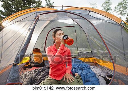 Stock Image - Mixed race woman drinking in tent. Fotosearch