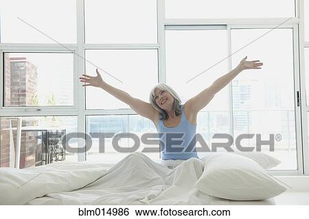 Stock Photograph - Smiling Caucasian woman sitting in bed. Fotosearch