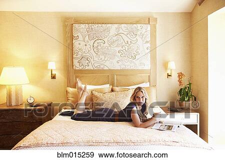 Stock Photo - Woman laying on bed in elegant bedroom. Fotosearch