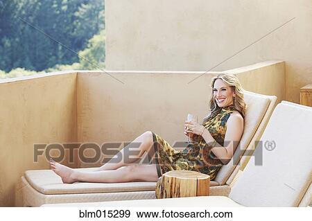 Stock Photo - Woman on lounge chair drinking wine. Fotosearch