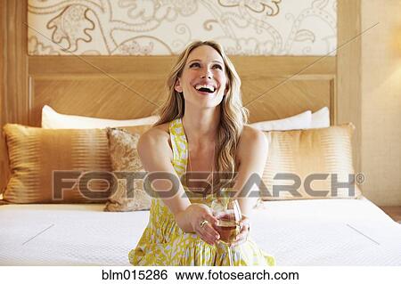 Stock Photograph - Woman sitting on bed drinking wine. Fotosearch