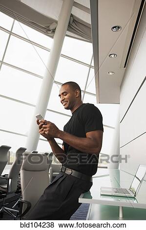 Stock Photo - Black businessman using cell phone in conference room. Fotosearch