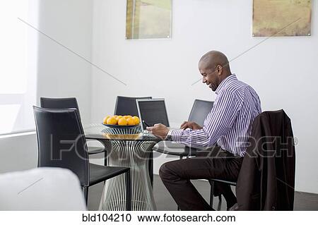 Stock Image - Black businessman using laptop and cell phone. Fotosearch