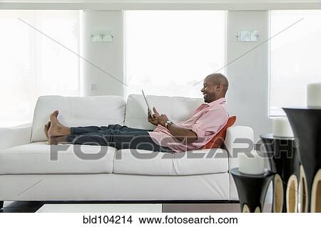 Black man on sofa using digital tablet View Large Photo Image Picture - Black man on sofa using digital tablet. Fotosearch