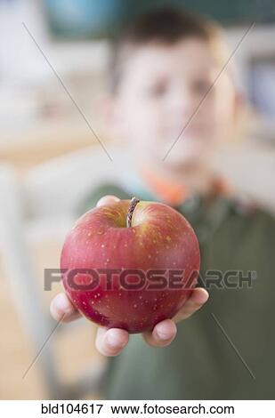 Stock Photo - Caucasian boy holding red apple in classroom. Fotosearch