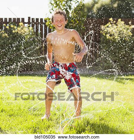 Stock Photography - Caucasian boy playing in sprinkler. Fotosearch