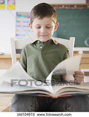 Stock Photography - Caucasian boy reading book in classroom. Fotosearch
