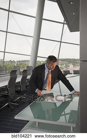 Stock Image - Caucasian businessman looking at paperwork in conference room. Fotosearch