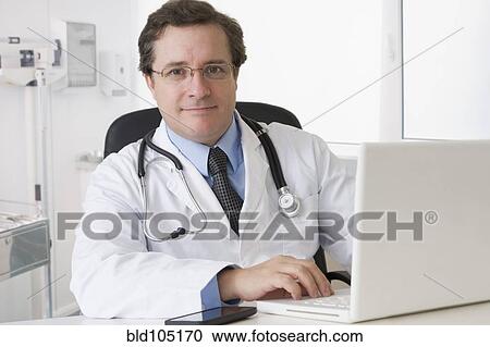 Caucasian doctor sitting at desk with laptop View Large Photo Image Stock Image - Caucasian doctor sitting at desk with laptop. Fotosearch