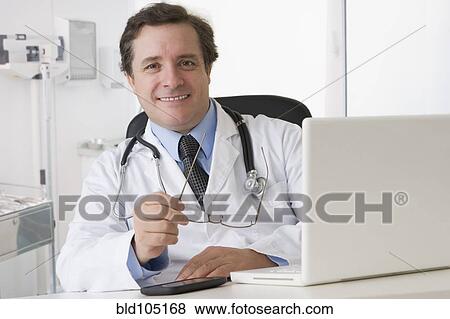 Stock Photo - Caucasian doctor sitting at desk with laptop. Fotosearch