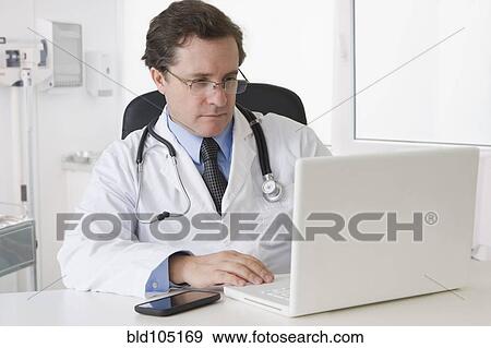 Stock Photo - Caucasian doctor sitting at desk with laptop. Fotosearch