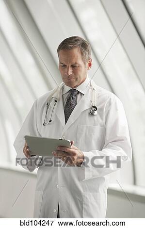 Caucasian doctor using digital tablet in hospital corridor View Large Photo Image Stock Photo - Caucasian doctor using digital tablet in hospital corridor. Fotosearch