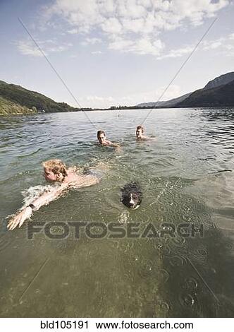 Stock Image - Caucasian friends swimming in lake with dog. Fotosearch