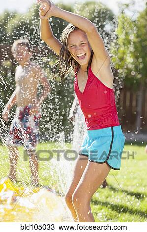 Stock Image - Caucasian girl playing in sprinkler. Fotosearch