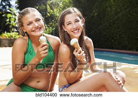 Stock Image - Caucasian girls eating ice cream cones near swimming pool. Fotosearch