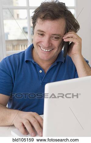Caucasian man using laptop and talking on cell phone View Large Photo Image Stock Photo - Caucasian man using laptop and talking on cell phone. Fotosearch