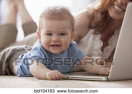 Stock Image - Caucasian mother and son using laptop on floor. Fotosearch