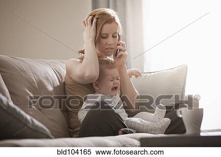 Stock Photography - Caucasian mother holding crying son and talking on cell phone. Fotosearch