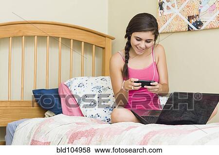 Stock Photo - Caucasian teenage girl with laptop text messaging on cell phone. Fotosearch