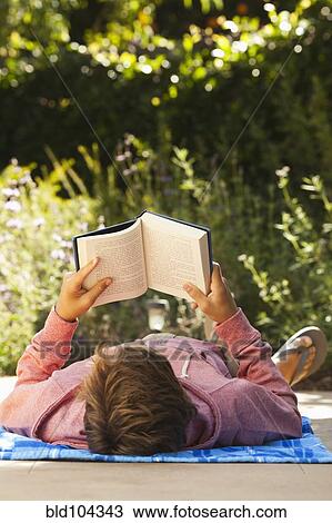 Stock Image - Caucasian teenager reading outdoors. Fotosearch