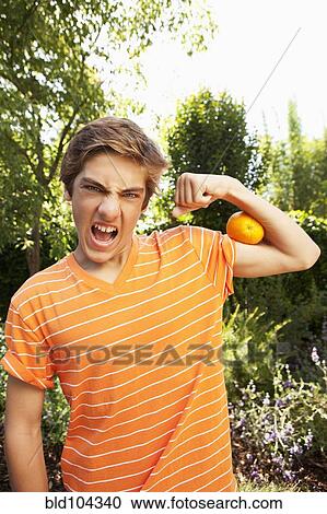 Stock Image - Caucasian teenager squeezing orange with arm. Fotosearch