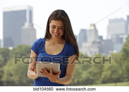 Stock Image - Caucasian woman using digital tablet in city park. Fotosearch