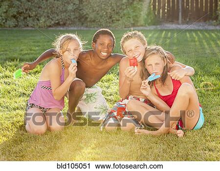 Stock Image - Children sitting in grass eating popsicles. Fotosearch
