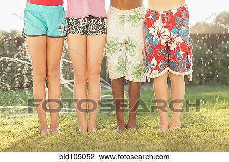 Stock Image - Children standing together in sprinkler. Fotosearch