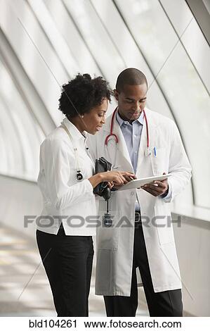 Stock Image - Doctors using digital tablet in hospital corridor. Fotosearch