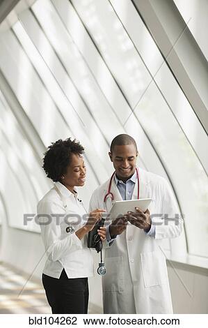 Stock Image - Doctors using digital tablet in hospital corridor. Fotosearch