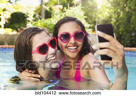 Stock Image - Friends in swimming pool looking at cell phone. Fotosearch