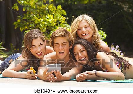 Picture - Friends laying outdoors together looking at cell phone. Fotosearch