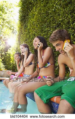 Friends sitting by pool talking on cell phones View Large Photo Image Picture - Friends sitting by pool talking on cell phones. Fotosearch
