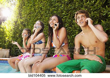 Stock Photography - Friends sitting by pool talking on cell phones. Fotosearch