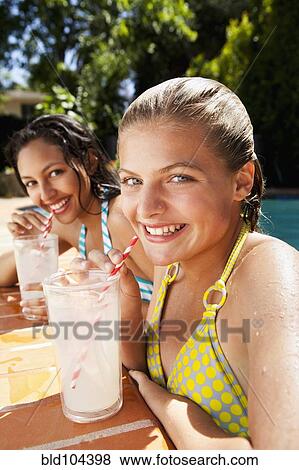 Stock Photo - Girls drinking lemonade near swimming pool. Fotosearch