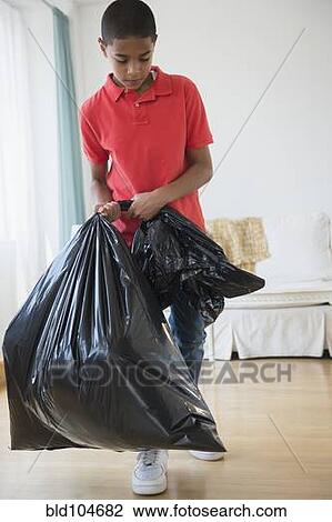 Stock Image - Hispanic boy carrying garbage bag. Fotosearch