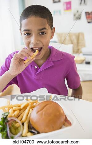 Stock Image - Hispanic boy eating hamburger and french fries. Fotosearch