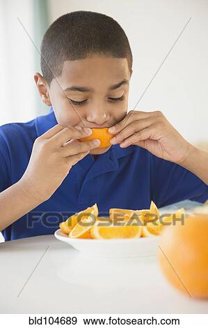 Stock Photo - Hispanic boy eating orange sections. Fotosearch