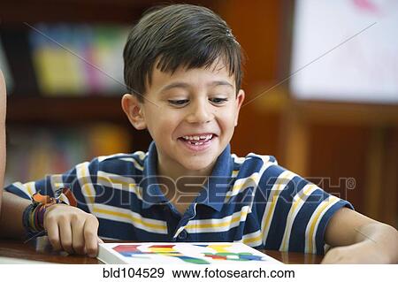 Stock Photo - Hispanic boy reading a book in library. Fotosearch
