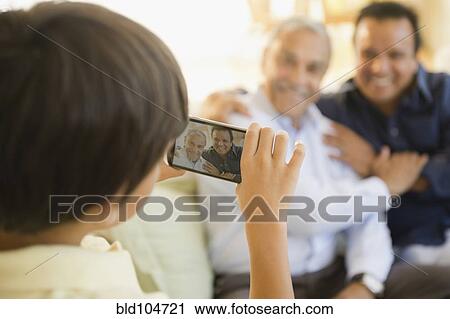 Stock Image - Hispanic boy taking photograph of father and grandfather. Fotosearch
