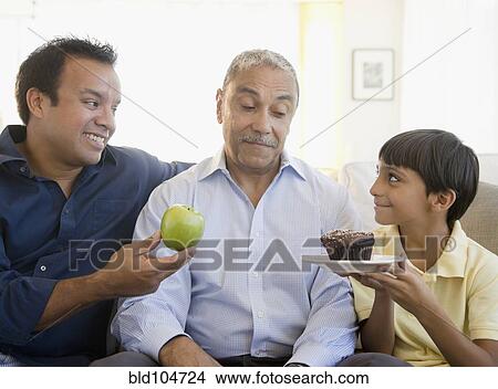 Hispanic father and son offering grandfather apple and cupcake View Large Photo Image Picture - Hispanic father and son offering grandfather apple and cupcake. Fotosearch