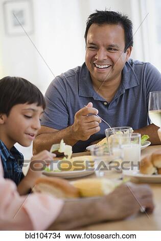 Picture - Hispanic grandfather, father and son eating dinner. Fotosearch